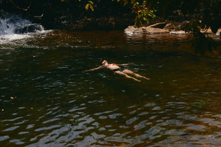 Person swimming in a natural water body with rocks and trees in the background